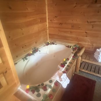 Cabin jacuzzi decorated with red rose petals and greenery inside a knotty pine log cabin